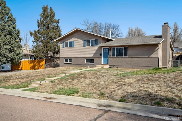 split level home with a chimney, fence, and brick siding