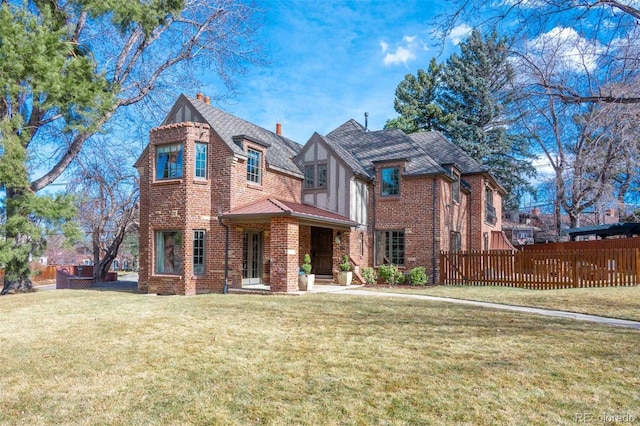 tudor house featuring a chimney, fence, a front lawn, and brick siding