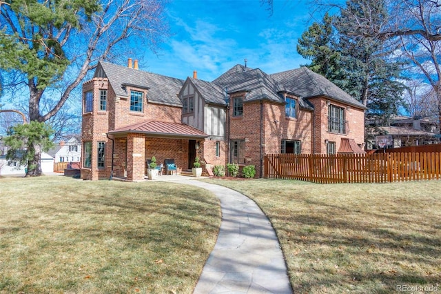 view of front facade with brick siding, a standing seam roof, a front yard, and fence