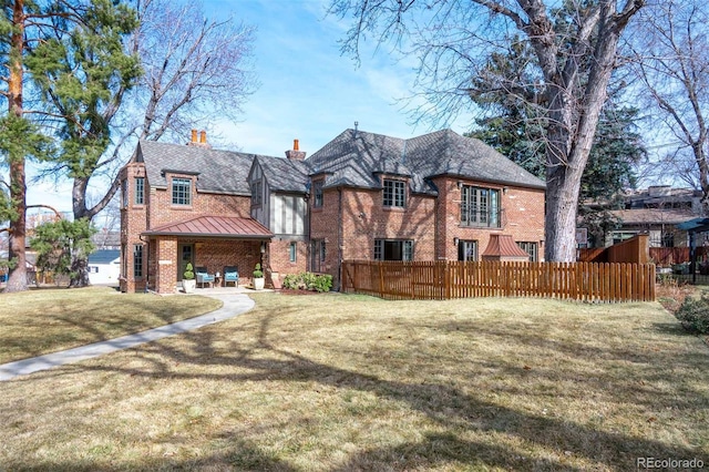 back of house with brick siding, fence, a chimney, and a lawn