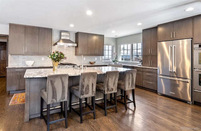 290 Dexter St, Denver, CO 80220 - kitchen with stainless steel appliances, wall chimney exhaust hood, decorative backsplash, a center island with sink, and a kitchen breakfast bar
