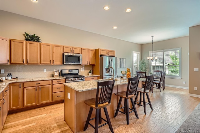 15852 Lavender Pl, Broomfield, CO 80023 - kitchen with appliances with stainless steel finishes, a chandelier, light wood-style floors, a kitchen island with sink, and light stone counters