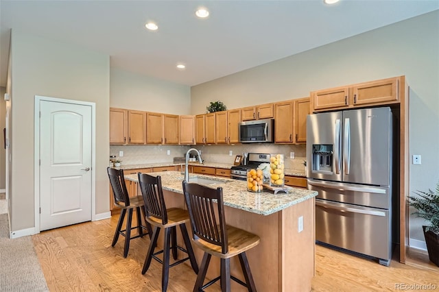 15852 Lavender Pl, Broomfield, CO 80023 - kitchen with appliances with stainless steel finishes, light stone countertops, light wood-style floors, a center island with sink, and a kitchen bar