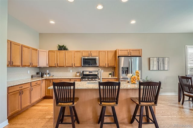 15852 Lavender Pl, Broomfield, CO 80023 - kitchen featuring appliances with stainless steel finishes, light wood finished floors, light stone counters, an island with sink, and recessed lighting