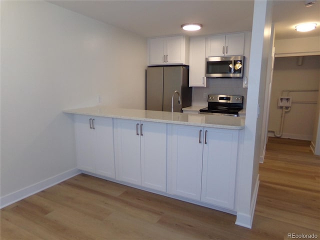 kitchen featuring appliances with stainless steel finishes, white cabinetry, light hardwood / wood-style floors, and backsplash