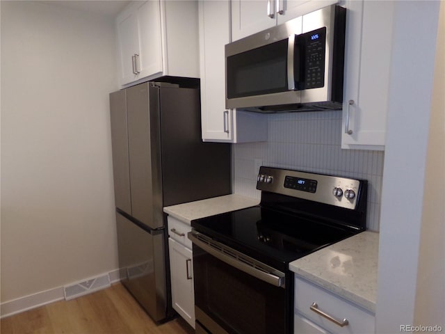 kitchen featuring white cabinets, stainless steel appliances, light stone countertops, and decorative backsplash