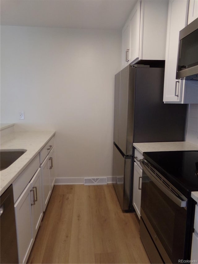 kitchen featuring light stone counters, white cabinets, appliances with stainless steel finishes, and light hardwood / wood-style floors