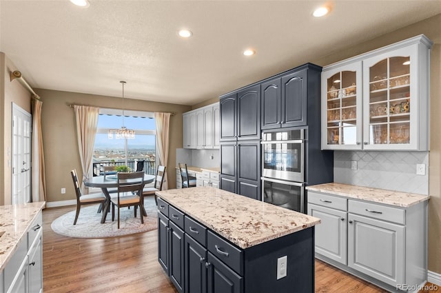 11991 Hazy Hills Dr, Parker, CO 80138 - kitchen featuring tasteful backsplash, light wood-type flooring, an inviting chandelier, glass insert cabinets, and stainless steel double oven
