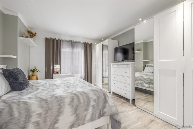bedroom featuring crown molding, light wood finished floors, and ensuite bath
