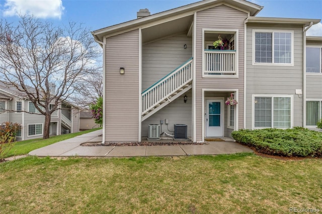 back of property featuring stairway, central air condition unit, and a yard