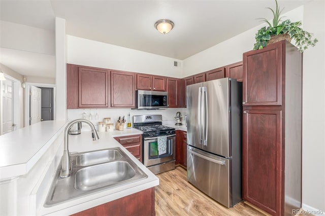 kitchen featuring stainless steel appliances, a sink, dark brown cabinets, a peninsula, and light countertops