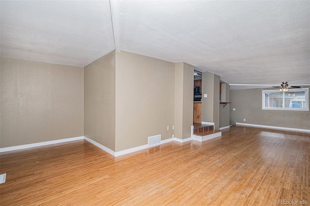 unfurnished living room with hardwood / wood-style floors, vaulted ceiling, a textured ceiling, and ceiling fan