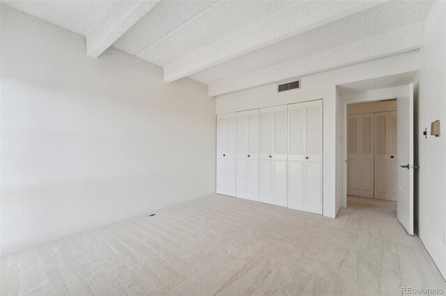 unfurnished bedroom with carpet floors, visible vents, a closet, and beamed ceiling