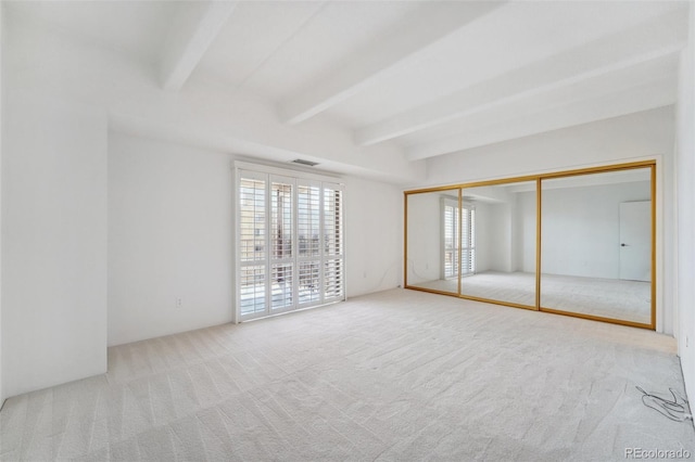 unfurnished bedroom featuring carpet floors, visible vents, beam ceiling, and a closet
