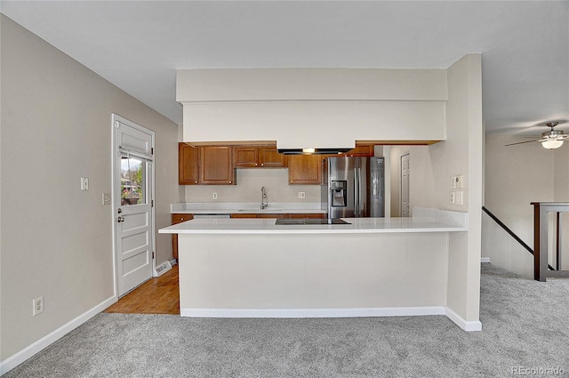 9099 W Harvard Pl, Lakewood, CO 80227 - kitchen with stainless steel fridge with ice dispenser, light carpet, light countertops, brown cabinetry, and a peninsula