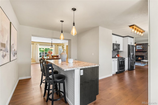 6858 Otis Ct, Arvada, CO 80003 - kitchen with stainless steel appliances, dark wood finished floors, a kitchen breakfast bar, white cabinetry, and hanging light fixtures