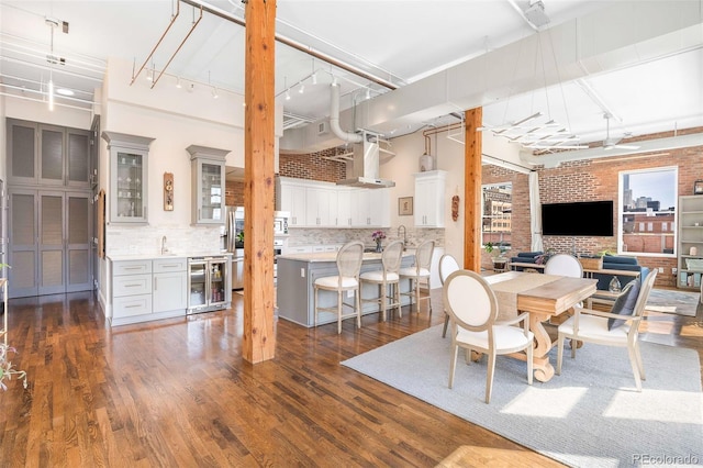 dining area featuring beverage cooler, track lighting, brick wall, and dark wood-style flooring