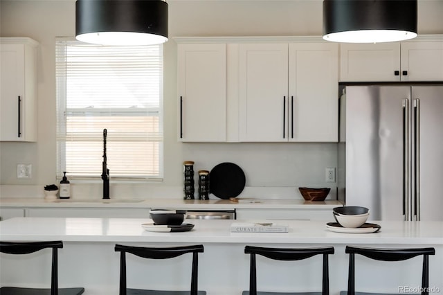 kitchen featuring high end fridge, a sink, a kitchen bar, light countertops, and white cabinets