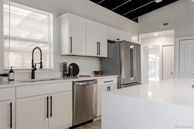 kitchen featuring appliances with stainless steel finishes, a sink, white cabinetry, plenty of natural light, and high vaulted ceiling