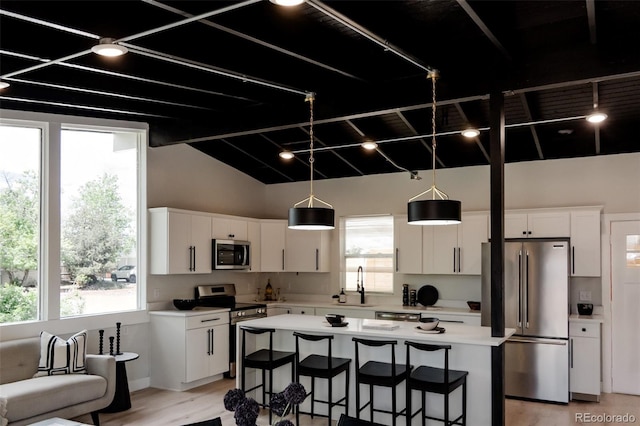 kitchen with stainless steel appliances, light countertops, white cabinetry, healthy amount of natural light, and vaulted ceiling