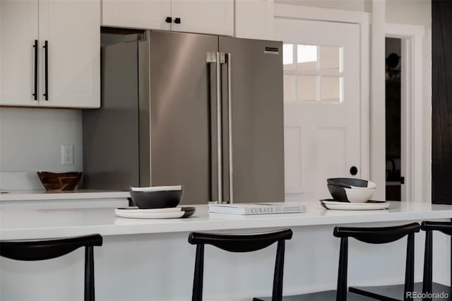 kitchen featuring high quality fridge, light countertops, white cabinets, and a kitchen bar