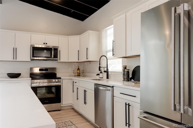 kitchen with stainless steel appliances, a sink, white cabinets, light countertops, and light wood finished floors