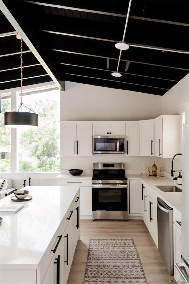 kitchen featuring appliances with stainless steel finishes, a sink, white cabinets, beamed ceiling, and light countertops