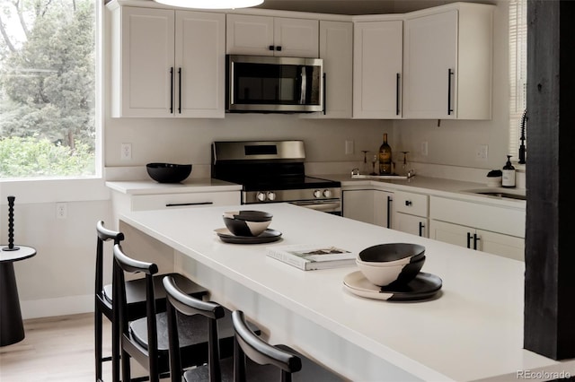 kitchen featuring stainless steel appliances, white cabinetry, light countertops, and light wood finished floors