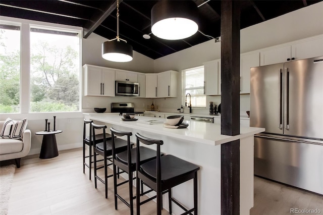 kitchen featuring stainless steel appliances, light countertops, a kitchen bar, white cabinets, and light wood-type flooring