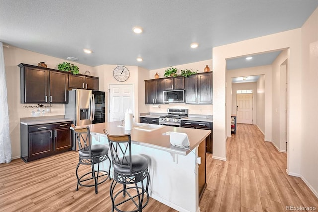 kitchen with a breakfast bar, a kitchen island with sink, stainless steel appliances, dark brown cabinets, and light hardwood / wood-style flooring