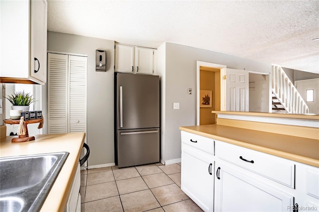 kitchen with stainless steel refrigerator, white cabinetry, sink, a textured ceiling, and light tile patterned floors