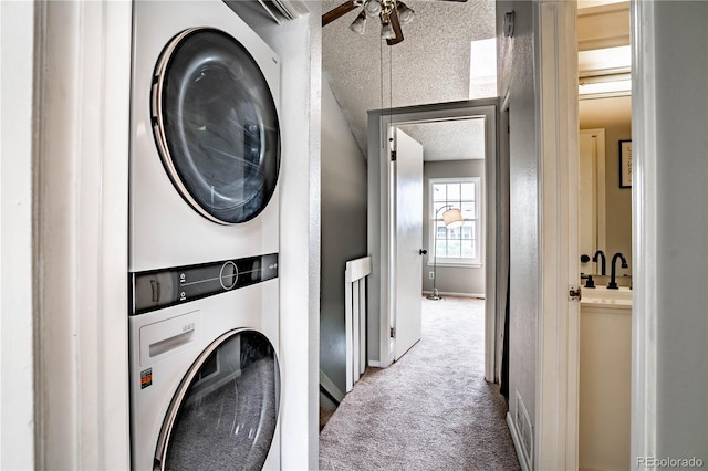 laundry room featuring ceiling fan, stacked washing maching and dryer, carpet floors, and a textured ceiling