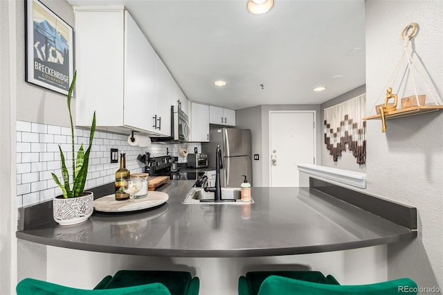 kitchen with white cabinets, sink, backsplash, stainless steel appliances, and a kitchen breakfast bar