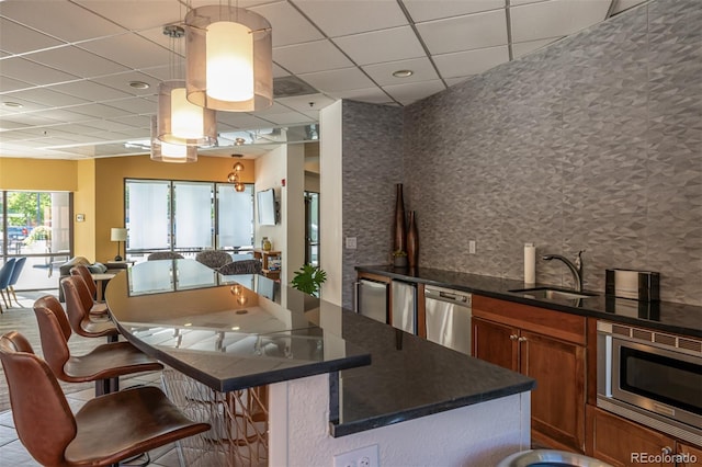 kitchen featuring a kitchen breakfast bar, pendant lighting, stainless steel appliances, a paneled ceiling, and sink