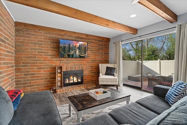 living area featuring a brick fireplace, brick wall, beam ceiling, and wood finished floors