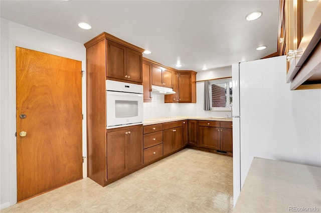 3022 Blackhawk St, Aurora, CO 80011 - kitchen featuring brown cabinetry, light countertops, under cabinet range hood, recessed lighting, and white appliances