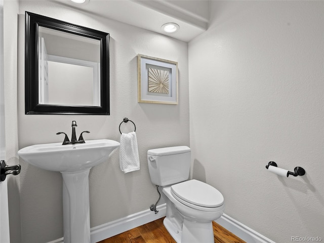bathroom featuring baseboards, wood finished floors, and toilet