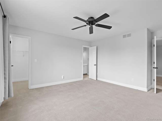 unfurnished bedroom with visible vents, baseboards, a walk in closet, and light colored carpet