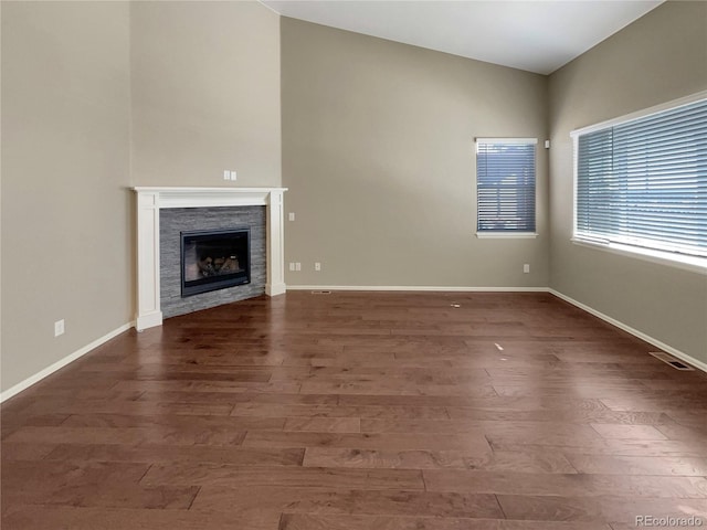 unfurnished living room with a fireplace, visible vents, vaulted ceiling, wood finished floors, and baseboards