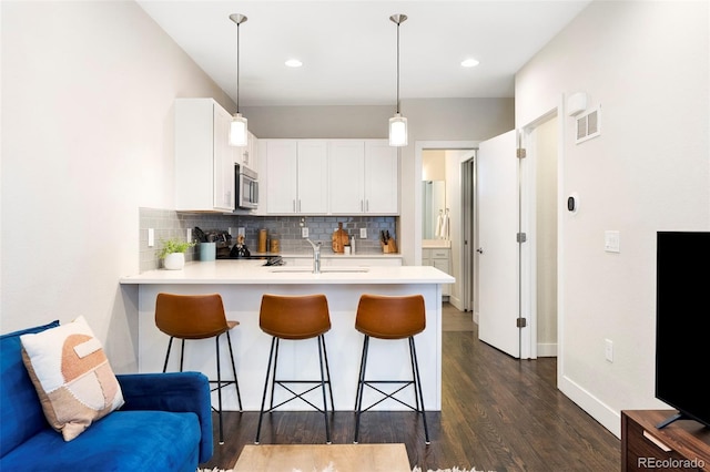 kitchen featuring stainless steel microwave, a peninsula, a sink, light countertops, and backsplash