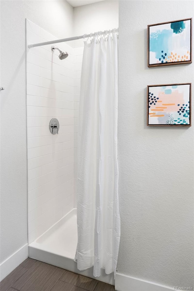 bathroom with a tile shower, baseboards, and wood finished floors