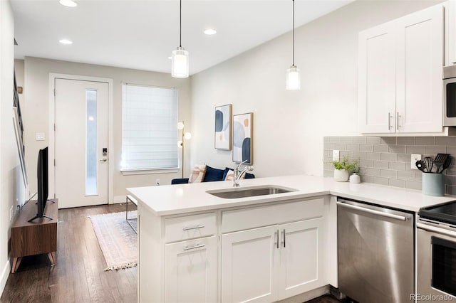 kitchen featuring appliances with stainless steel finishes, dark wood-style flooring, a peninsula, light countertops, and a sink