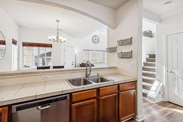 kitchen with stainless steel dishwasher, sink, decorative light fixtures, light wood-type flooring, and an inviting chandelier