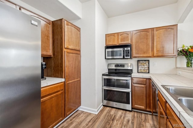 kitchen with light wood-type flooring, tile counters, appliances with stainless steel finishes, and sink