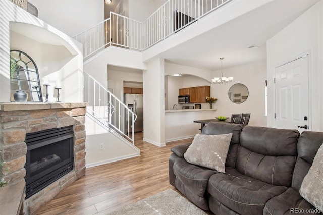 living room featuring a fireplace, light hardwood / wood-style floors, a high ceiling, and a notable chandelier