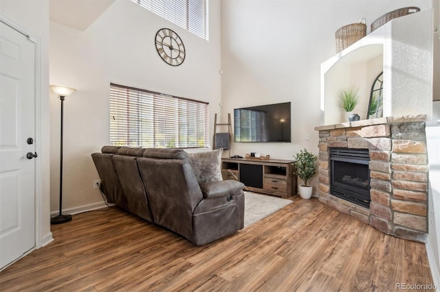 living room with wood-type flooring, a towering ceiling, and a fireplace