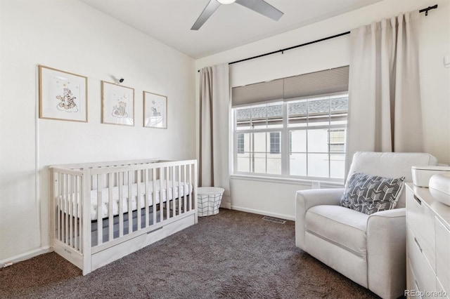 carpeted bedroom with a crib and ceiling fan