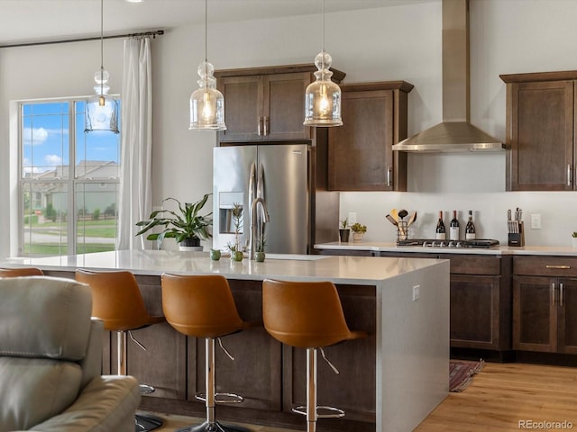 2113 Fountain Cir, Erie, CO 80516 - kitchen featuring wall chimney exhaust hood, appliances with stainless steel finishes, an island with sink, light countertops, and a kitchen bar