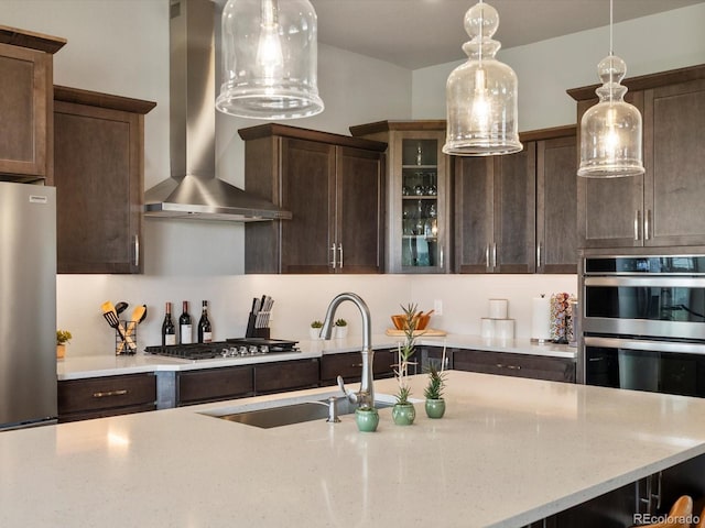 2113 Fountain Cir, Erie, CO 80516 - kitchen with wall chimney range hood, appliances with stainless steel finishes, dark brown cabinetry, pendant lighting, and glass insert cabinets