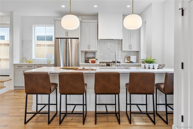 kitchen featuring custom exhaust hood, stainless steel fridge, decorative light fixtures, light hardwood / wood-style floors, and a breakfast bar area